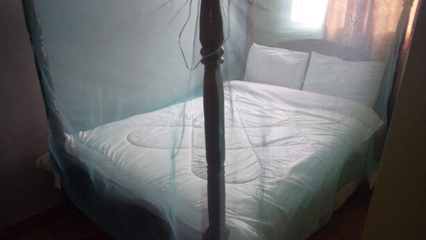 A bed with a mosquito net, a wooden headboard, and a white mattress. - The Plateau Breeze Hotel (Ruiru)