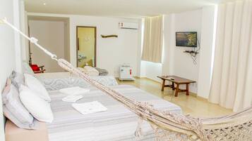 A hotel room with a bed, a hammock, a desk, a chair, a television, and a window with curtains.