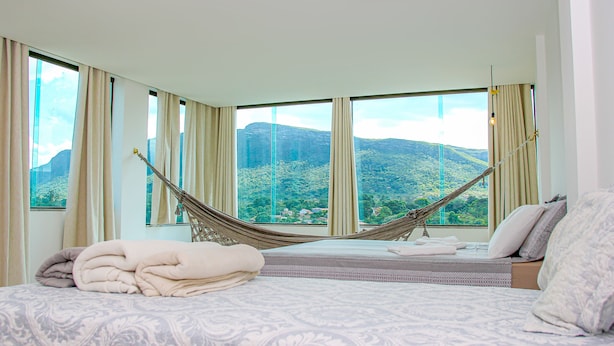 A bedroom with a large bed, a hammock, and a view of a mountainous landscape through large windows. - Pousada Vie (Palmeiras)