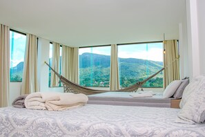 Une chambre dotée d’un grand lit, d’un hamac et offrant une vue sur un paysage montagneux grâce à de grandes fenêtres.