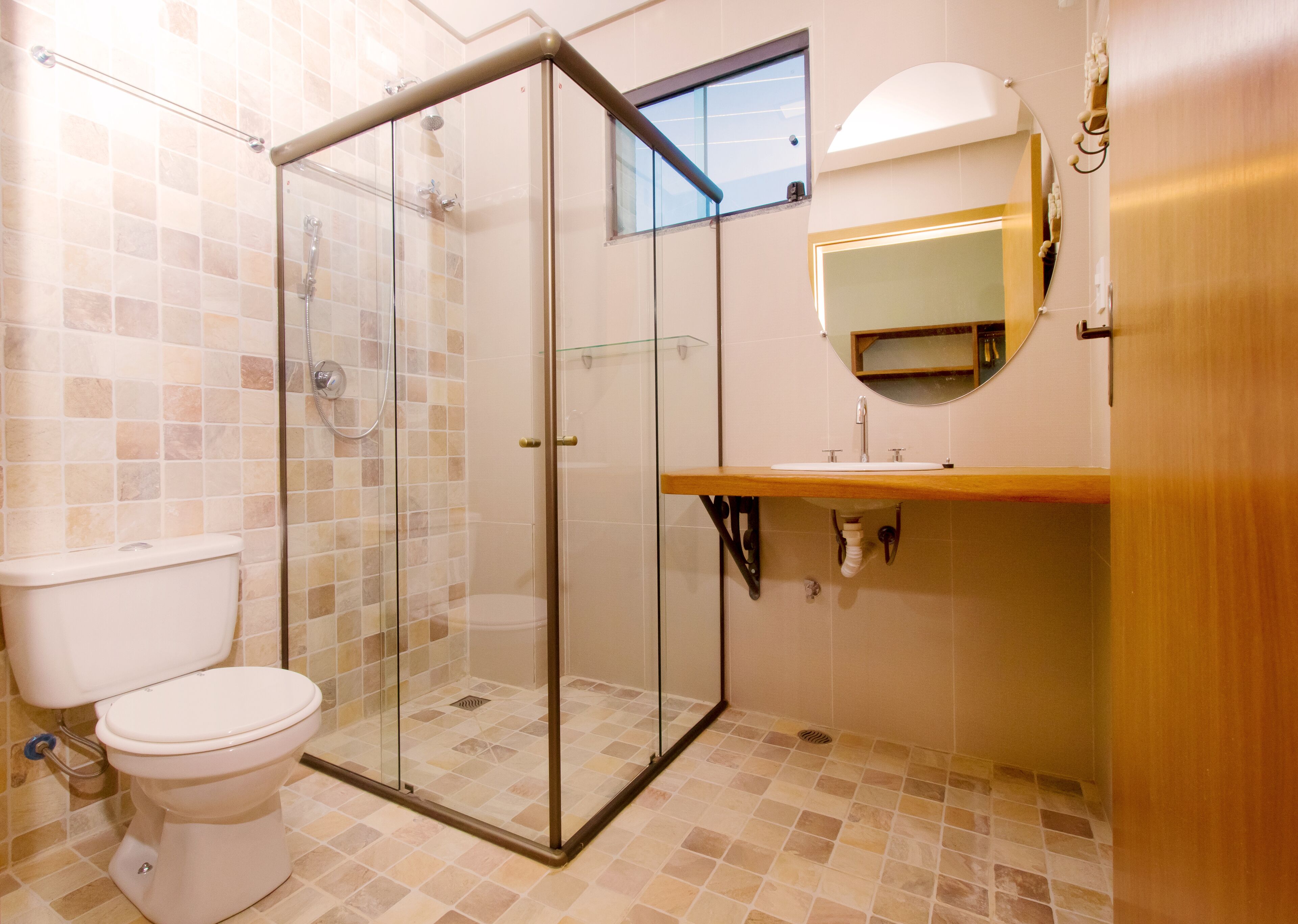 A bathroom with a glass-enclosed shower, a toilet, a sink with a mirror above it, and tiled flooring.