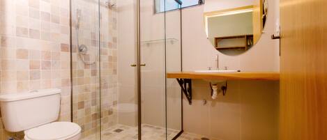 A bathroom with a glass-enclosed shower, a toilet, a sink with a mirror above it, and tiled flooring.
