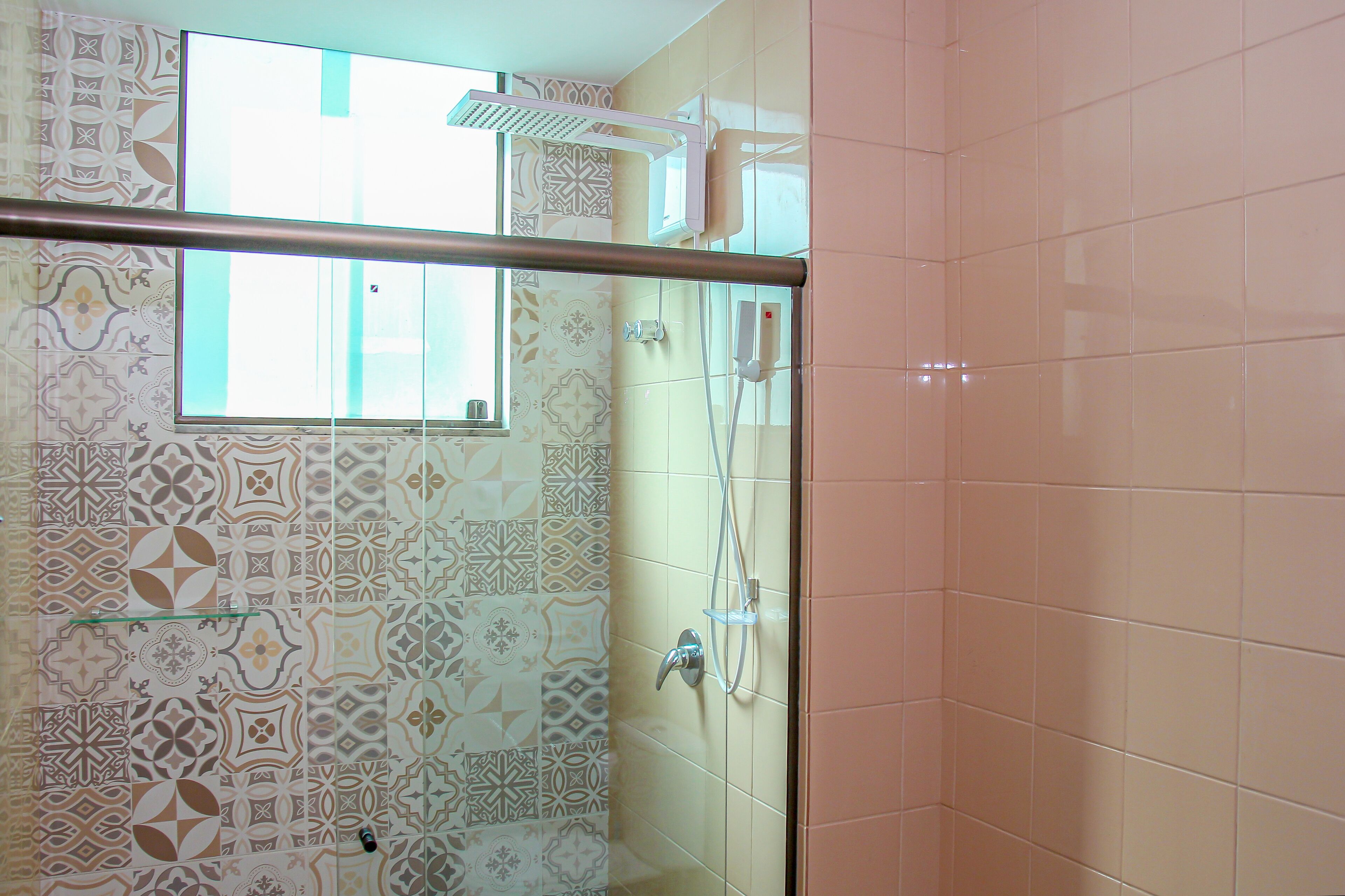 A shower area with patterned tiles, a glass shelf, and a window.