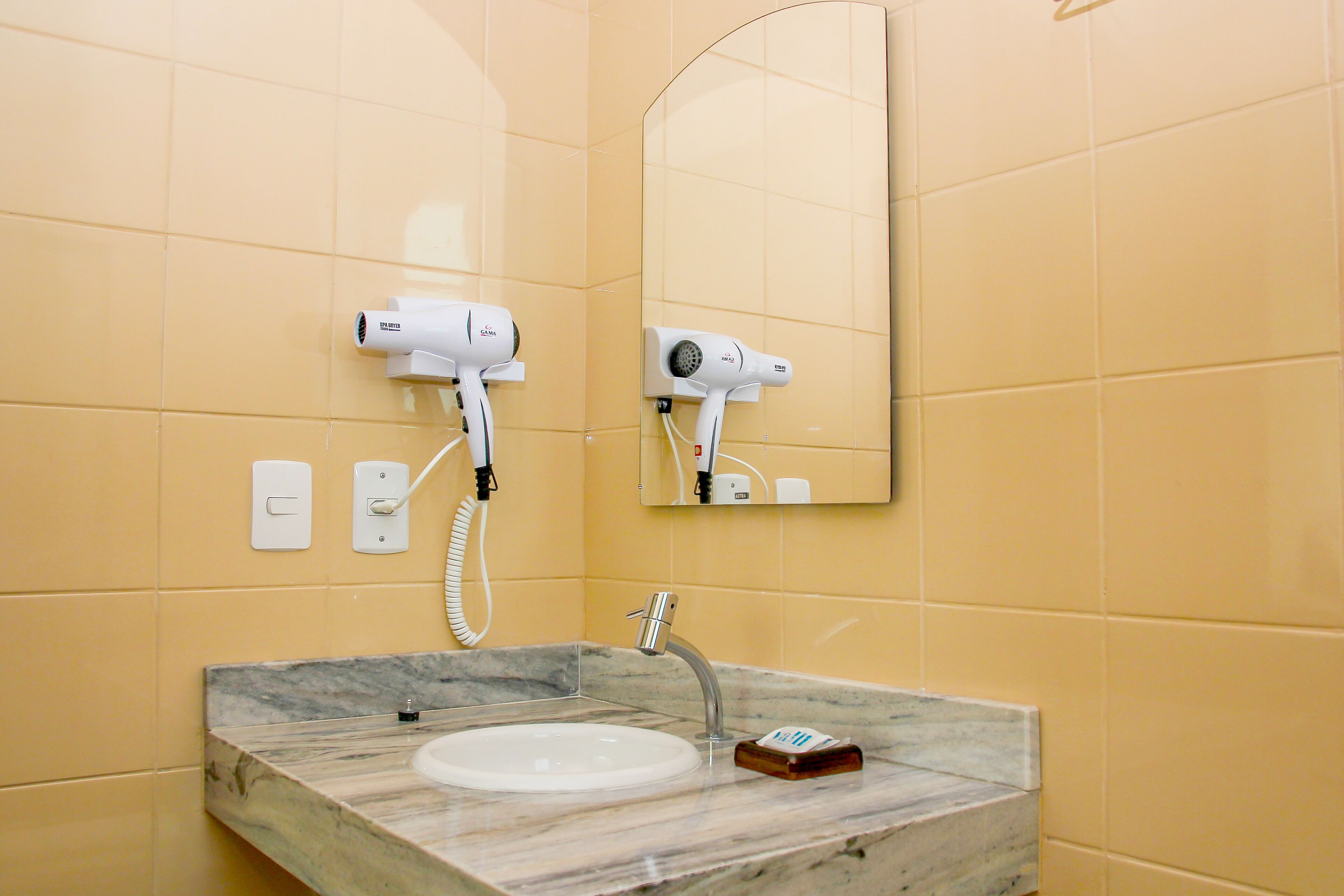 A bathroom with a marble sink, two wall-mounted hair dryers, and a mirror.