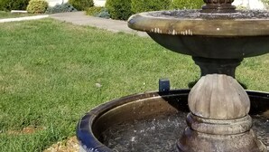 Una fuente frente a una casa de fachada blanca y techo gris.