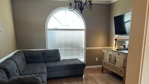Una sala de estar con un sofá modular, piso de madera, un televisor y un aparador.
