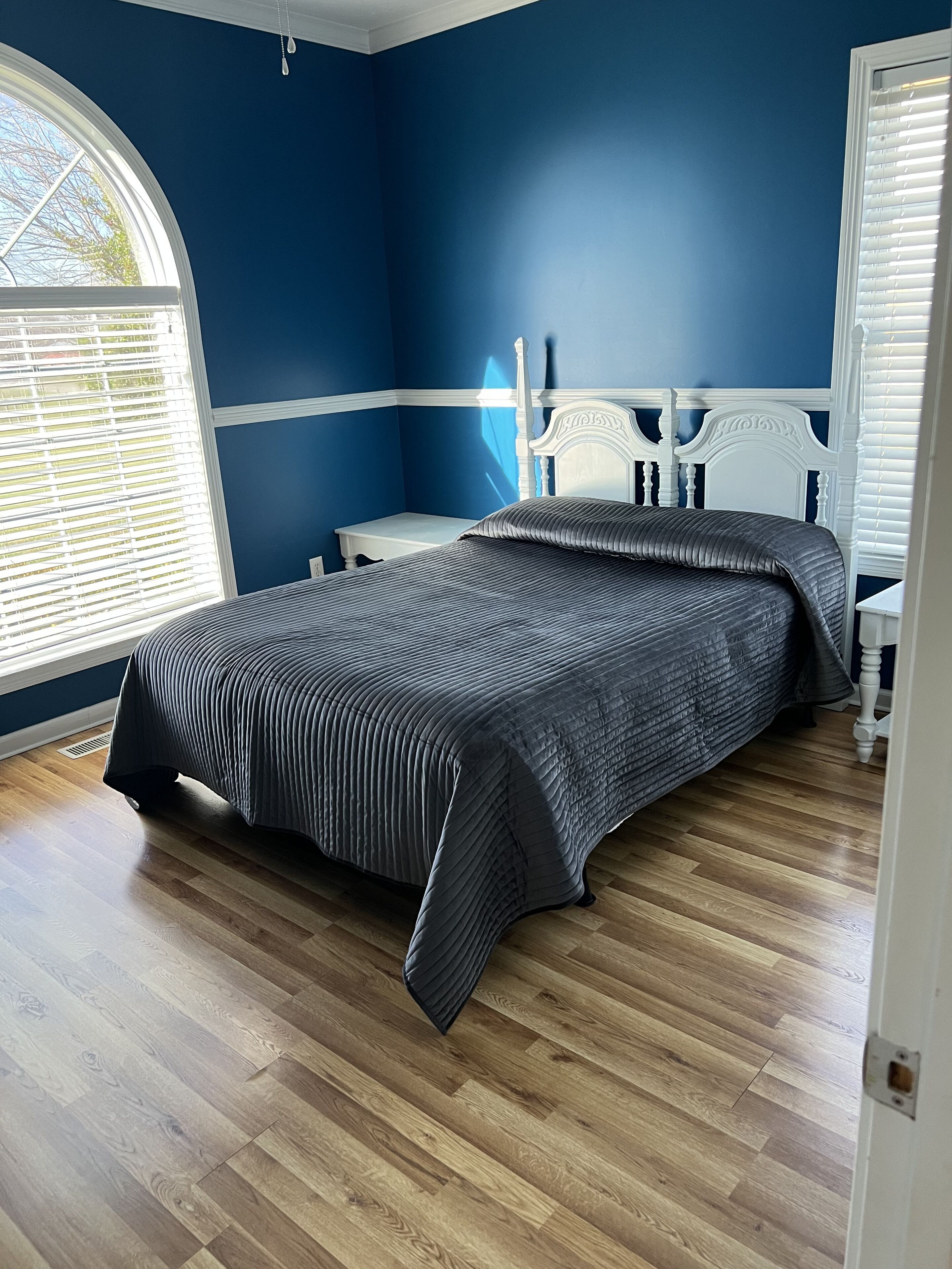 A bedroom with a bed, a nightstand, and a window with blinds.