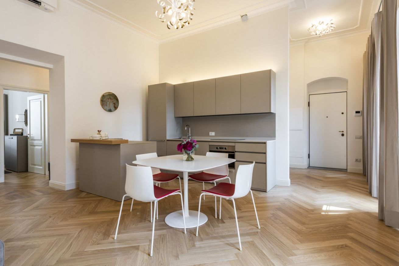 A modern kitchen with a dining area, featuring a white table with red chairs, a built-in oven, and a large cabinet above the counter.