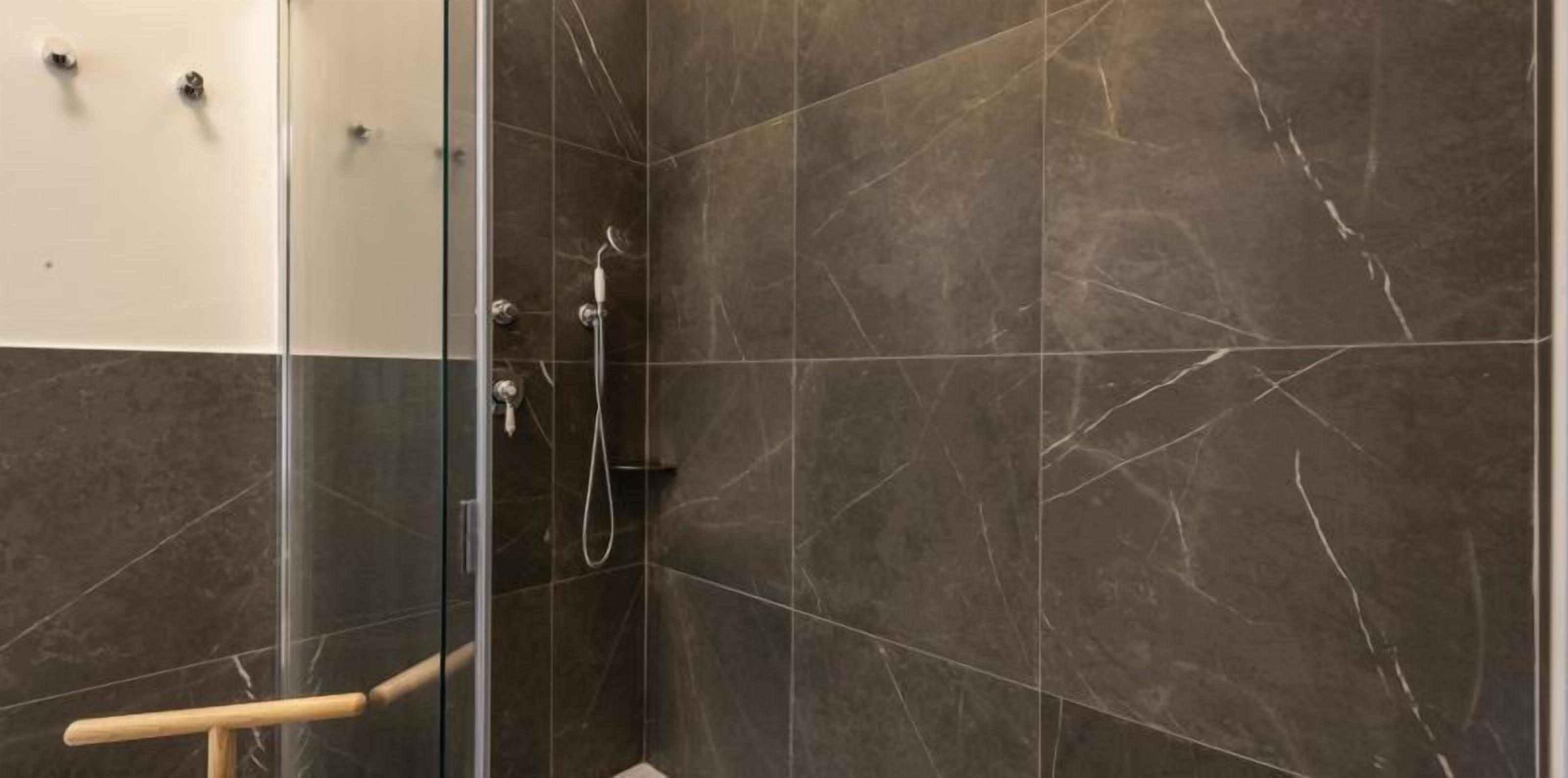 A shower area with dark marble tiles and a glass door.