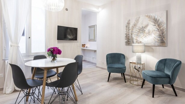 Un salon moderne avec une table à manger ronde, deux fauteuils bleus, une lampe blanche et un grand tableau abstrait accroché au mur.