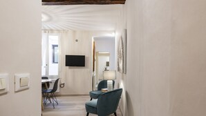 Une chambre d’hôtel équipée d’un téléviseur à écran plat fixé au mur, d’un coin repas avec une table et des chaises, et d’un espace détente avec un fauteuil et une lampe.