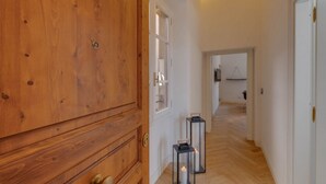 Un pasillo con suelo de madera, una puerta de madera y dos faroles negros con velas.