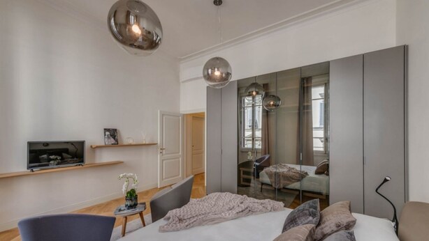 Un dormitorio moderno con una cama grande, un televisor en un estante, una silla y un espejo.