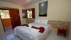 Une chambre d’hôtel avec un lit, une porte en bois, une fenêtre, un tableau accroché au mur et une petite table de chevet en bois.
