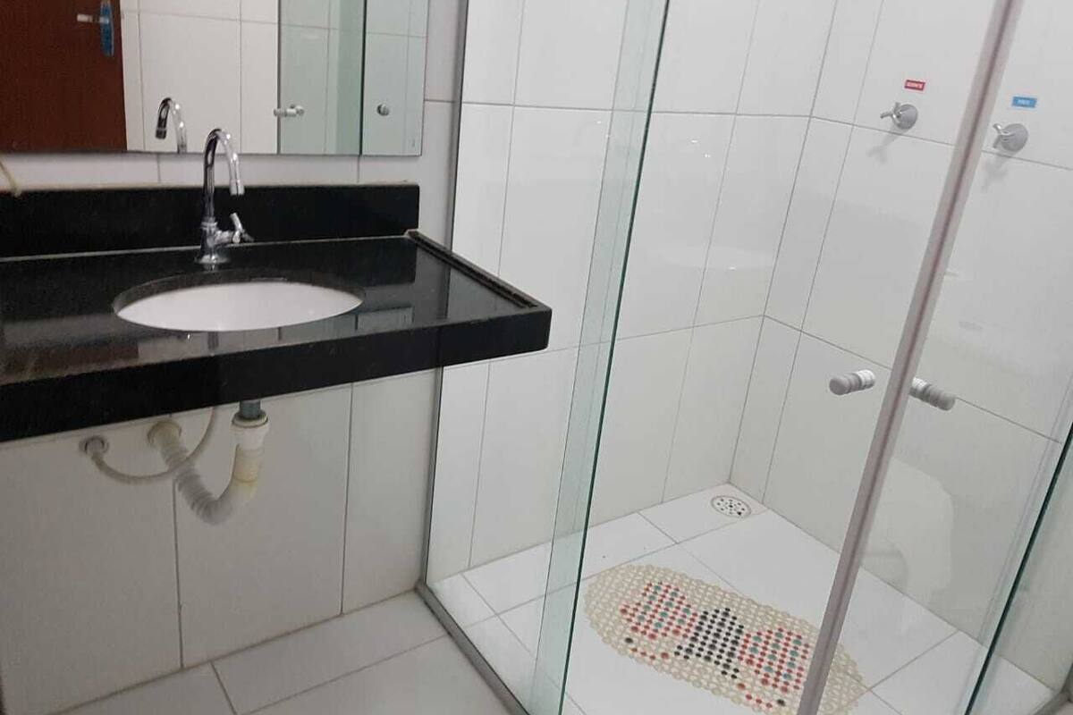 Un baño con lavamanos de superficie negra, un espejo y una cabina de ducha con mampara de vidrio.