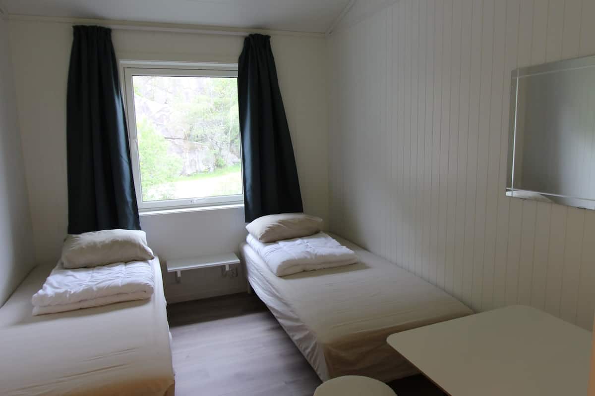 A small, clean room with two single beds, a small table, and a window with curtains.