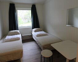 A small, clean room with two single beds, a small table, and a window with curtains.