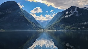A serene lake with mountains on either side, clear skies, and calm water reflecting the surroundings. - Trolltunga Camping (Ullensvang)