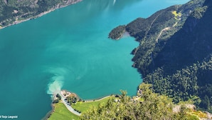 A mountainous landscape with a turquoise lake, a waterfall, and a winding road. - Trolltunga Camping (Ullensvang)