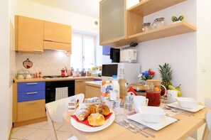 A kitchen with wooden cabinets, a microwave, and a dining table set with breakfast items. - Al Duomo (Trento)