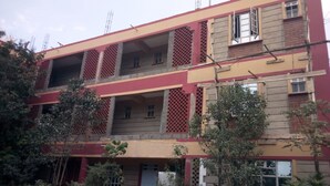 Un immeuble à plusieurs étages, doté d’une façade rouge et beige, de nombreux balcons et d’une entrée centrale.