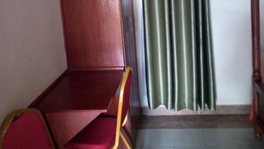 Une pièce avec un bureau en bois et deux chaises rouges, un rideau vert et un cadre de lit en bois.