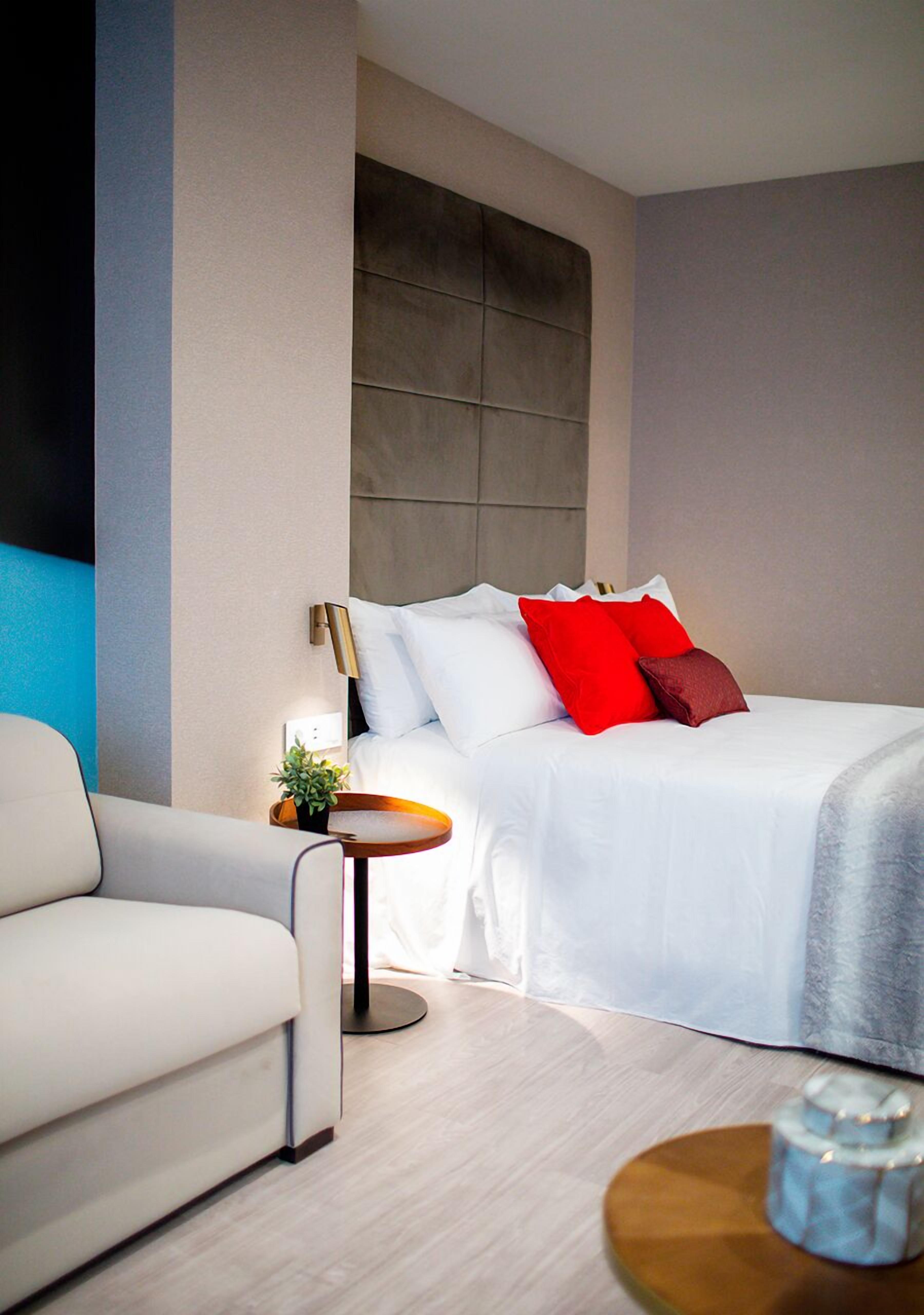 Ein modernes Hotelzimmer mit einem Bett, einem Sofa und einem kleinen Tisch mit einer Lampe.