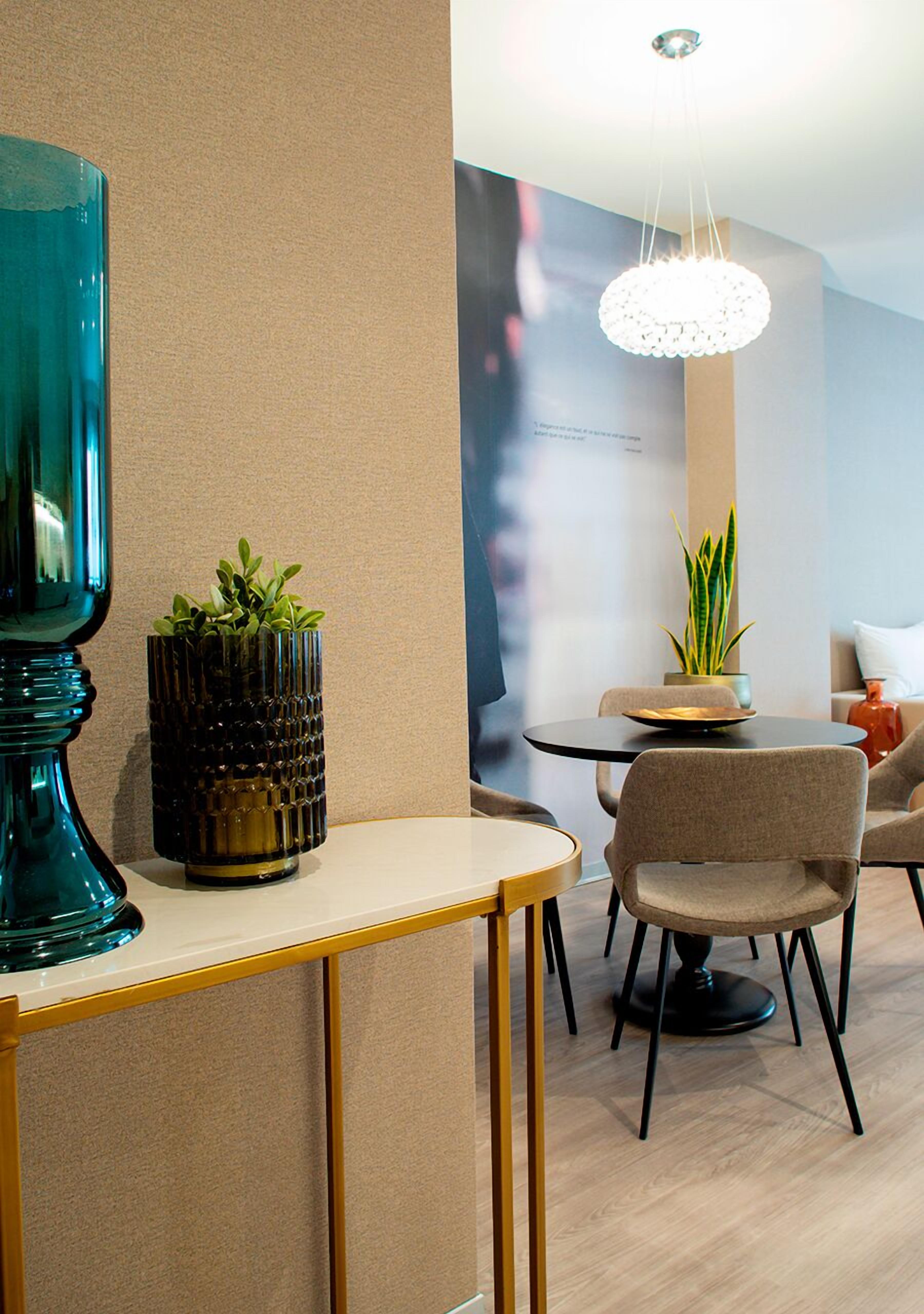 A modern interior with a round table, chairs, a potted plant, and a decorative light fixture.