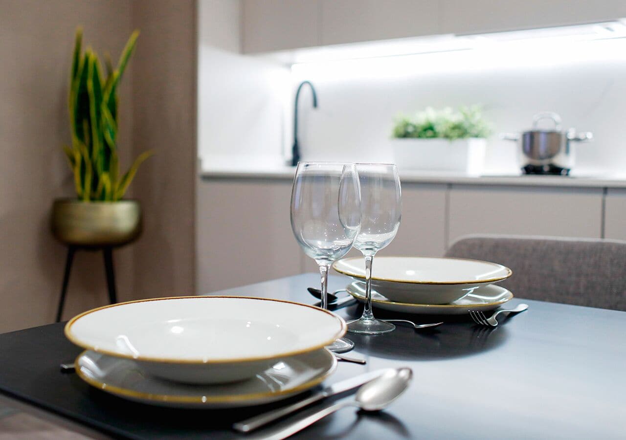 Una mesa de comedor dispuesta con platos, copas de vino, una cuchara y un cuchillo.