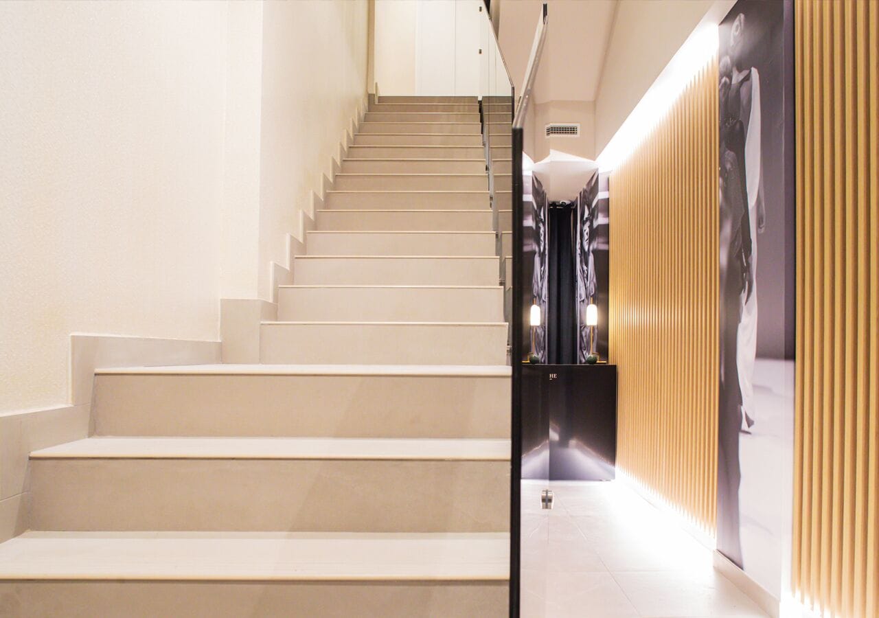 A modern staircase with a minimalist design, leading to a well-lit area with a patterned wall and a framed picture.