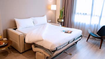Una habitación de hotel con cama, mesita de noche, lámpara, planta en maceta y una silla.