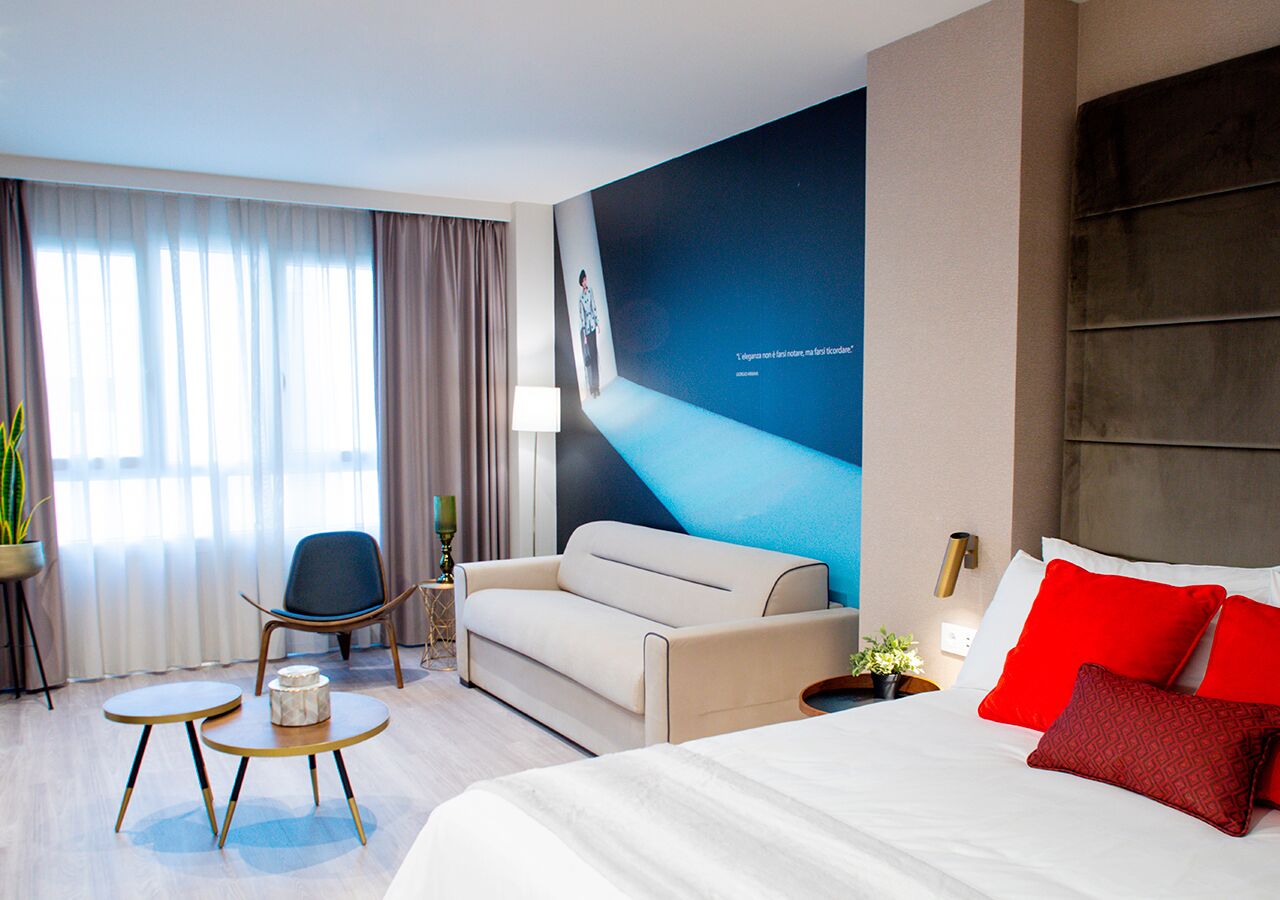 Una habitación de hotel moderna con una cama grande, un sofá, una mesita y una silla.
