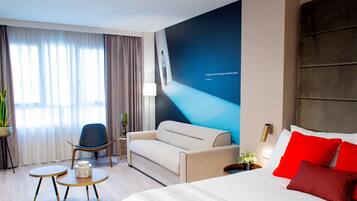 Una habitación de hotel moderna con una cama grande, un sofá, una mesita y una silla.