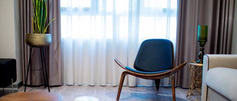 A modern living room with a blue chair, a sofa, a small round table, and a potted plant.
