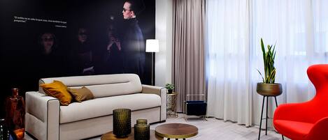 Una sala de estar moderna con un sofá, dos mesas redondas, una silla roja y un ventanal con cortinas.