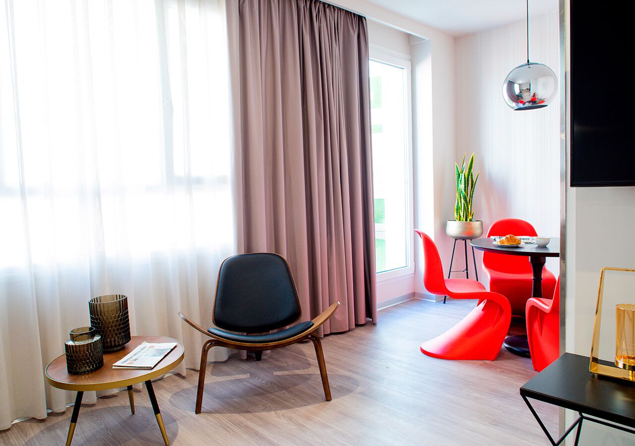 Una sala de estar moderna con suelo de madera, una silla negra, una pequeña mesa redonda con un periódico y una silla roja.