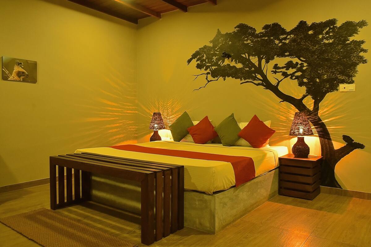 Een slaapkamer met een bed, nachtkastjes, een spiegel en een decoratieve boom aan de muur.
