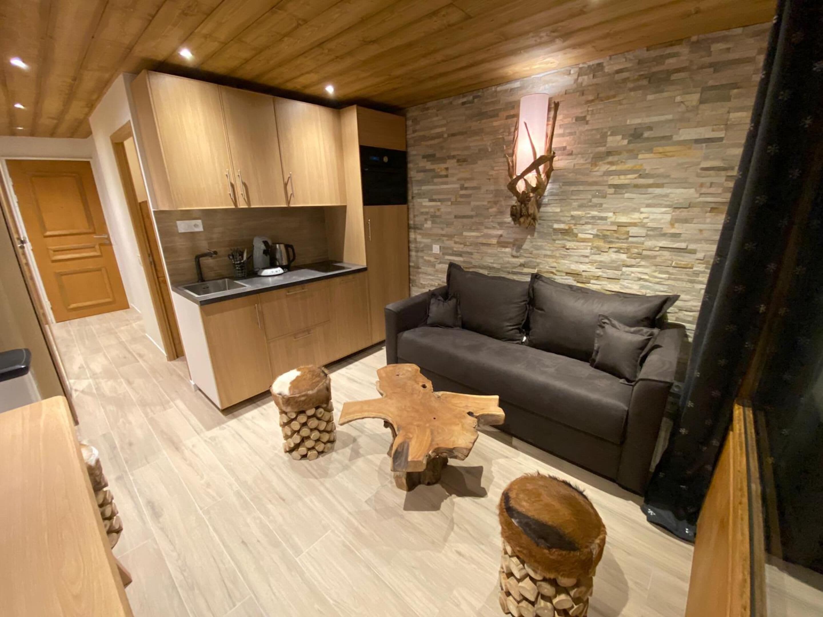 Una cocina moderna con armarios de madera y una pared de piedra. Hay un sofá gris y una mesa de centro con patas de madera.