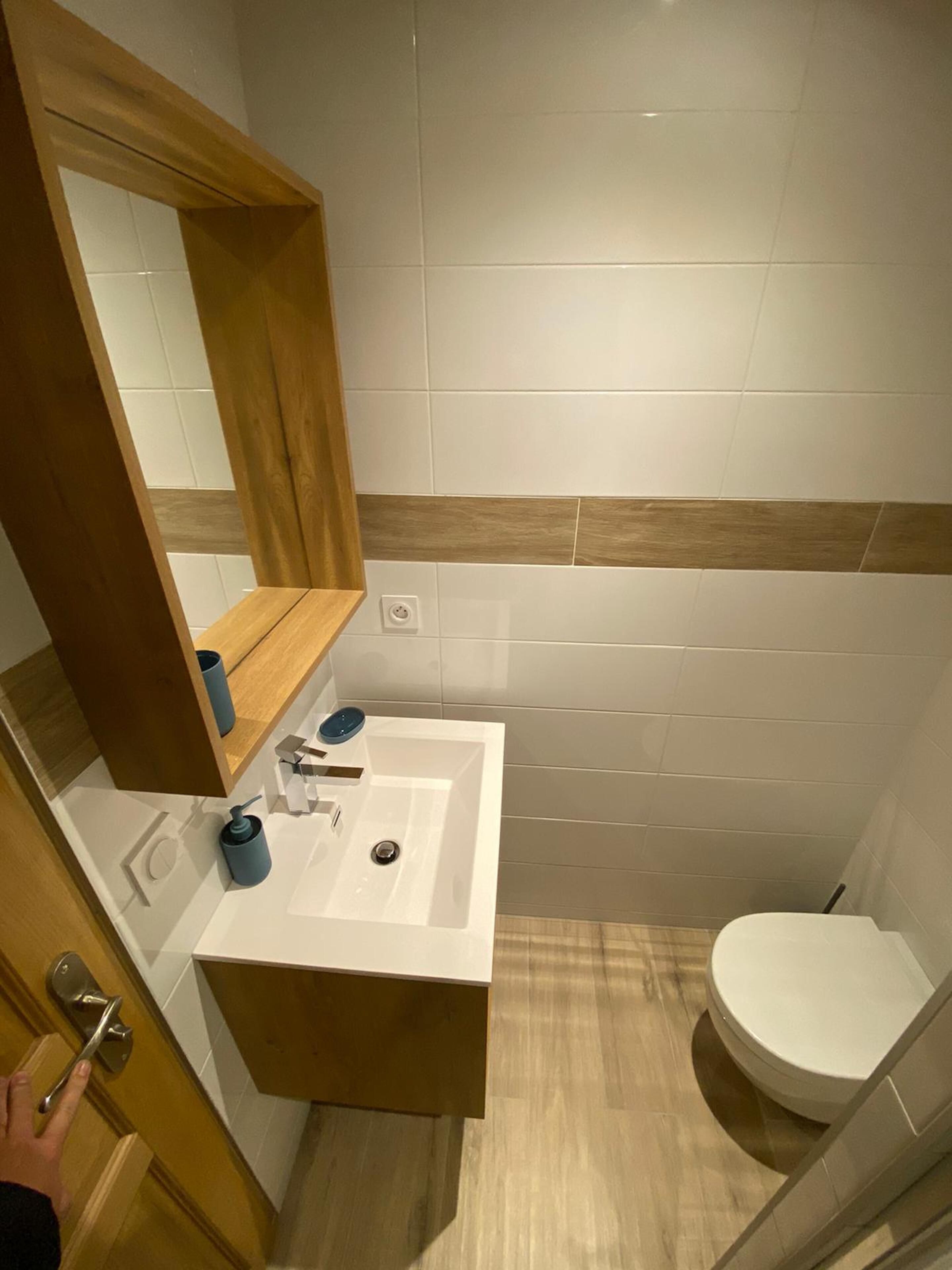 A bathroom with a wooden vanity, a mirror, a sink, and a toilet.