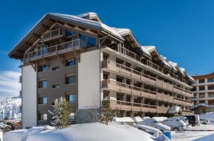 Un hotel de varios pisos con balcones y una pista de esquí al fondo.