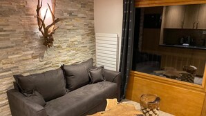 A modern living room with a stone wall, a leather sofa, a wooden coffee table, and a fireplace with a deer head decoration. - Résidence La Forêt Du Praz (Courchevel)