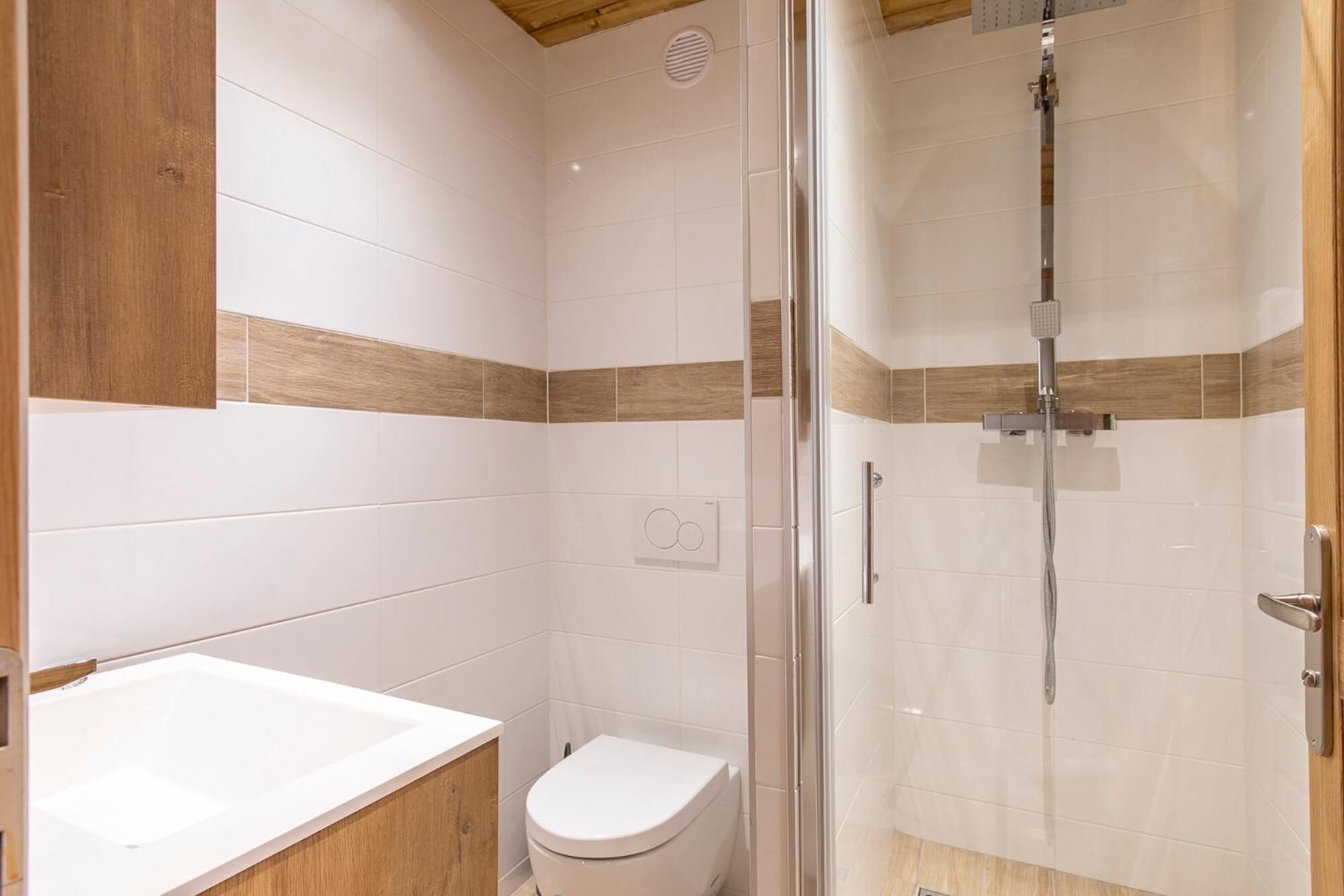 A modern bathroom with a glass shower enclosure, a white toilet, and a wooden vanity with a white sink.
