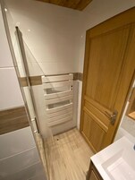 Un baño con ducha, una puerta de madera y un lavamanos blanco.