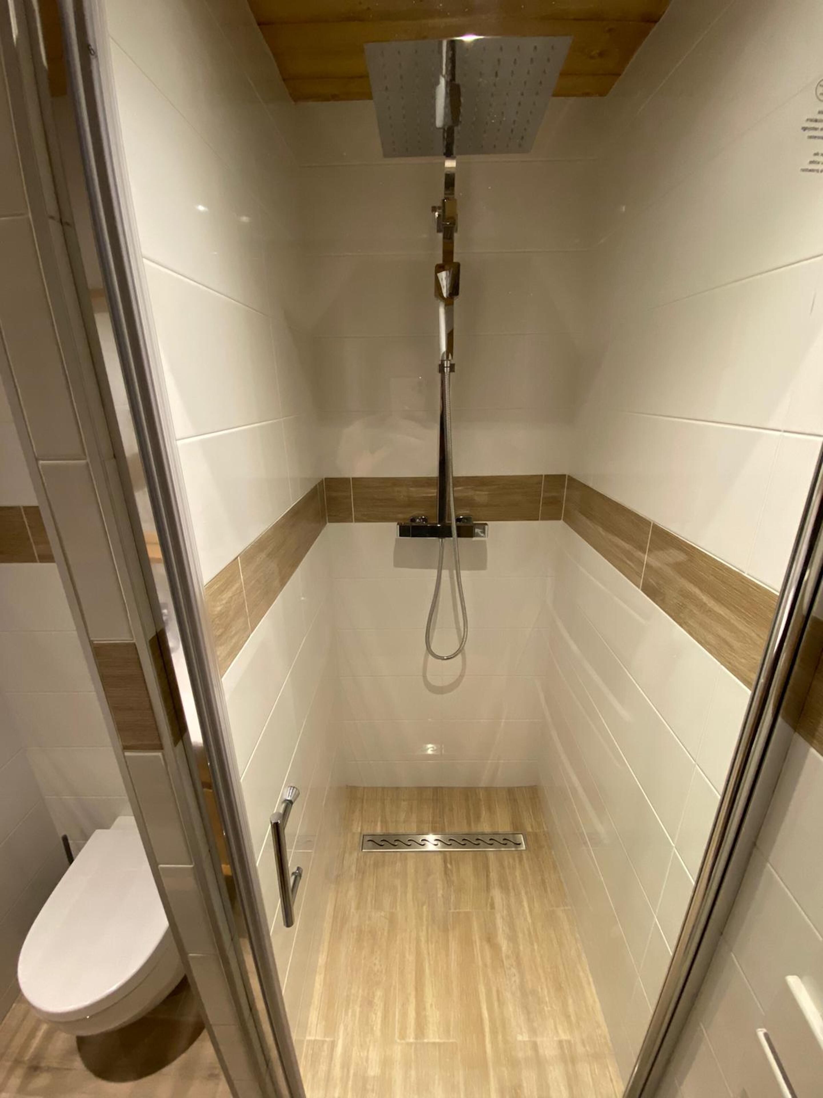 A small, enclosed shower stall with a glass door, a showerhead, and a toilet.