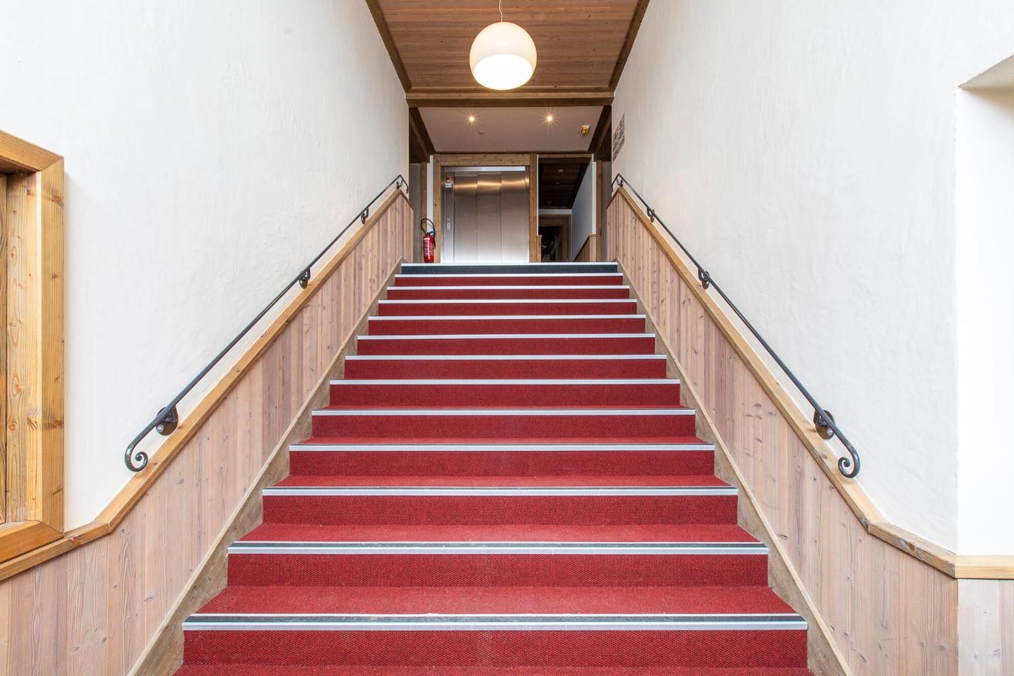 A staircase with red carpeted steps, wooden handrails, and a wooden ceiling.