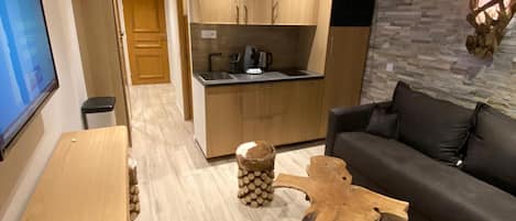 Una sala moderna con suelo de madera, un sofá negro, una mesa de centro de madera y un televisor a la izquierda.