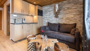 A modern kitchen with wooden cabinets and a stone backsplash, a cozy living area with a sofa and a coffee table, and a rustic wooden coffee table with logs. - Résidence La Forêt Du Praz (Courchevel)