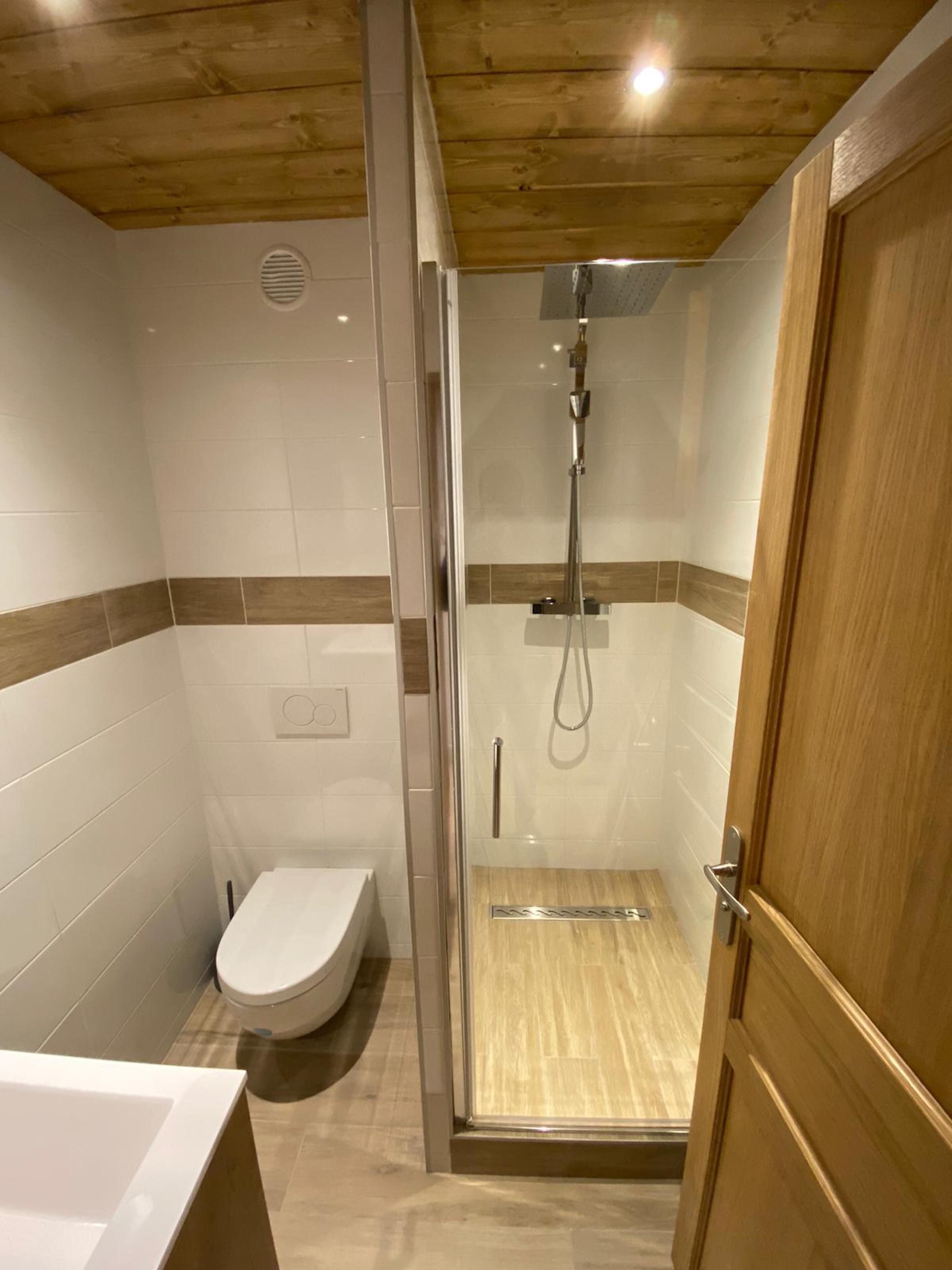 Un baño moderno con ducha envuelta en vidrio, inodoro y puerta de madera.