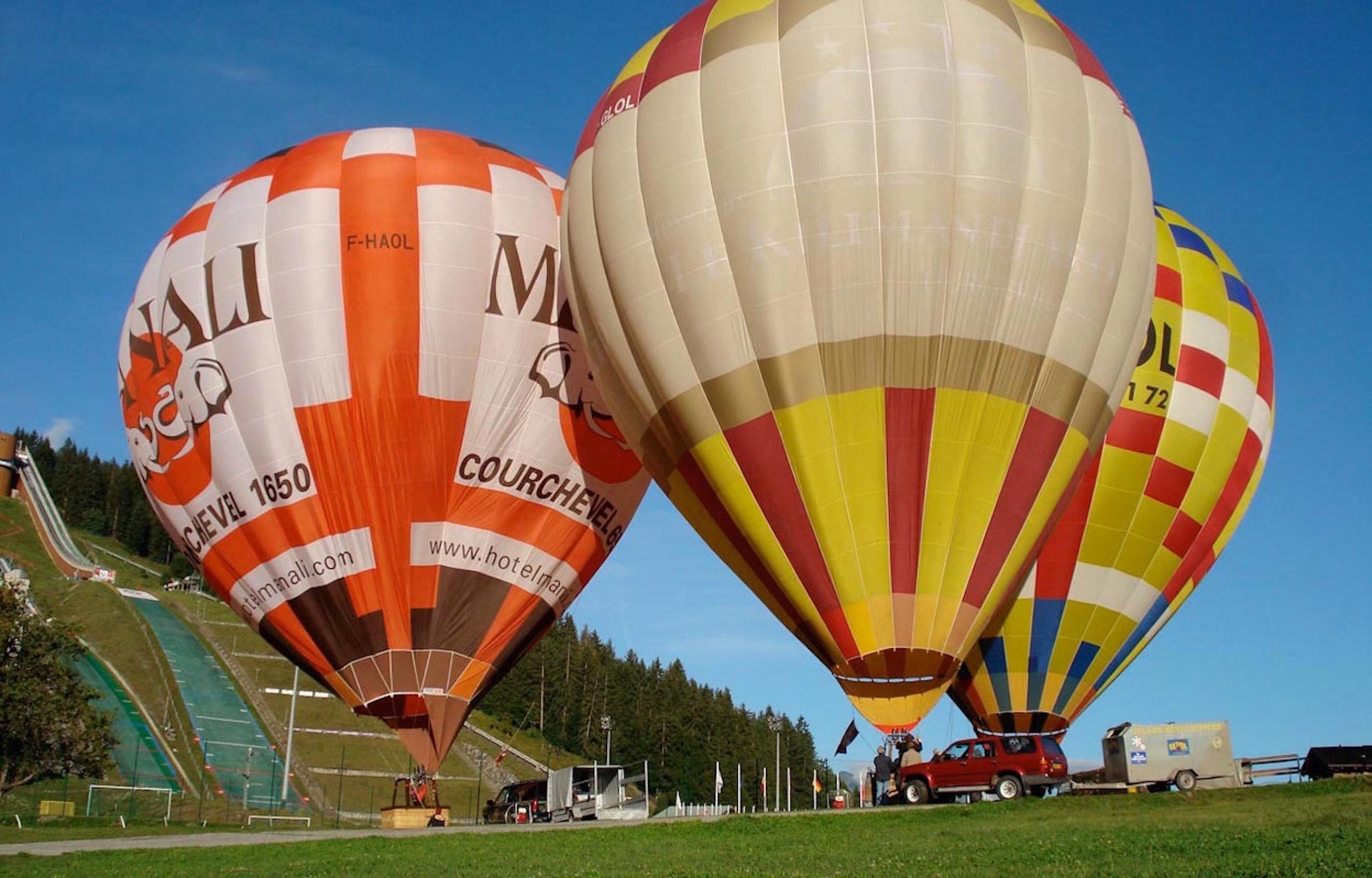 Two hot air balloons with visible text and logos, parked on a grassy field with a clear sky.