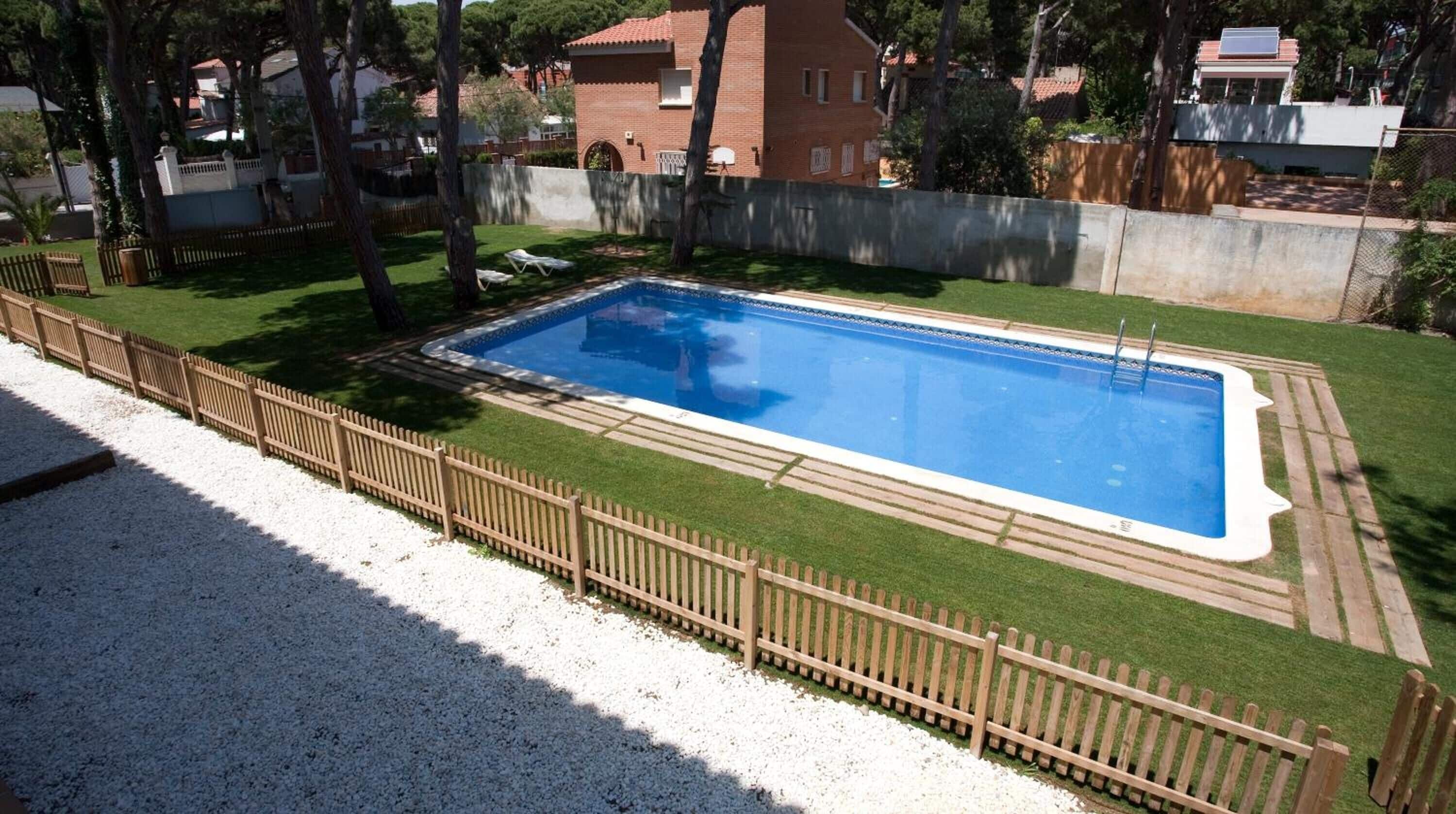 A rectangular swimming pool with a wooden deck and a fence surrounding it.